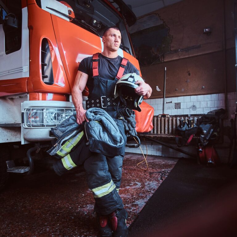 Fireman wearing protective uniform standing next to a fire engine in a garage of a fire department